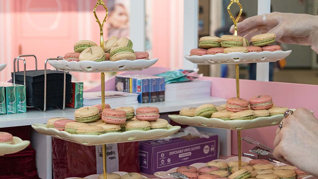 Three-tiered dessert stand with colorful macarons on a pink table.